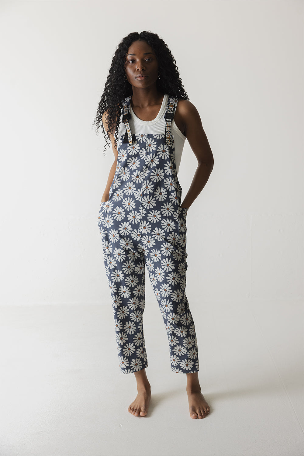 Women's overalls with white daisy pattern on navy background, paired with white tank top