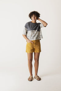 Mustard yellow corduroy shorts worn with patterned top, full body view on model