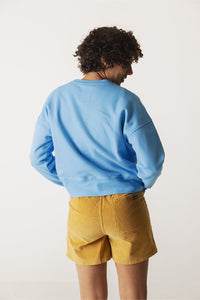 Mustard yellow corduroy shorts shown from back view on model with blue sweatshirt