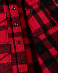 Close-up detail of red and black plaid wool shirt showing buttons, chest pocket, and fabric texture
