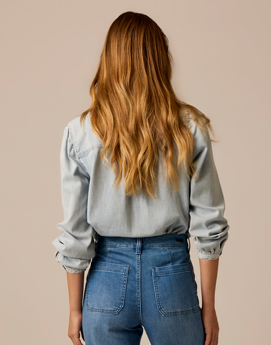 Women's lightweight denim shirt back view, long sleeves rolled at cuffs, paired with blue jeans