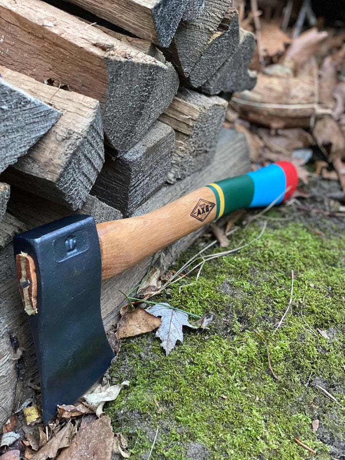 Small camping hatchet with colorful striped wooden handle lying on mossy ground near split wood
