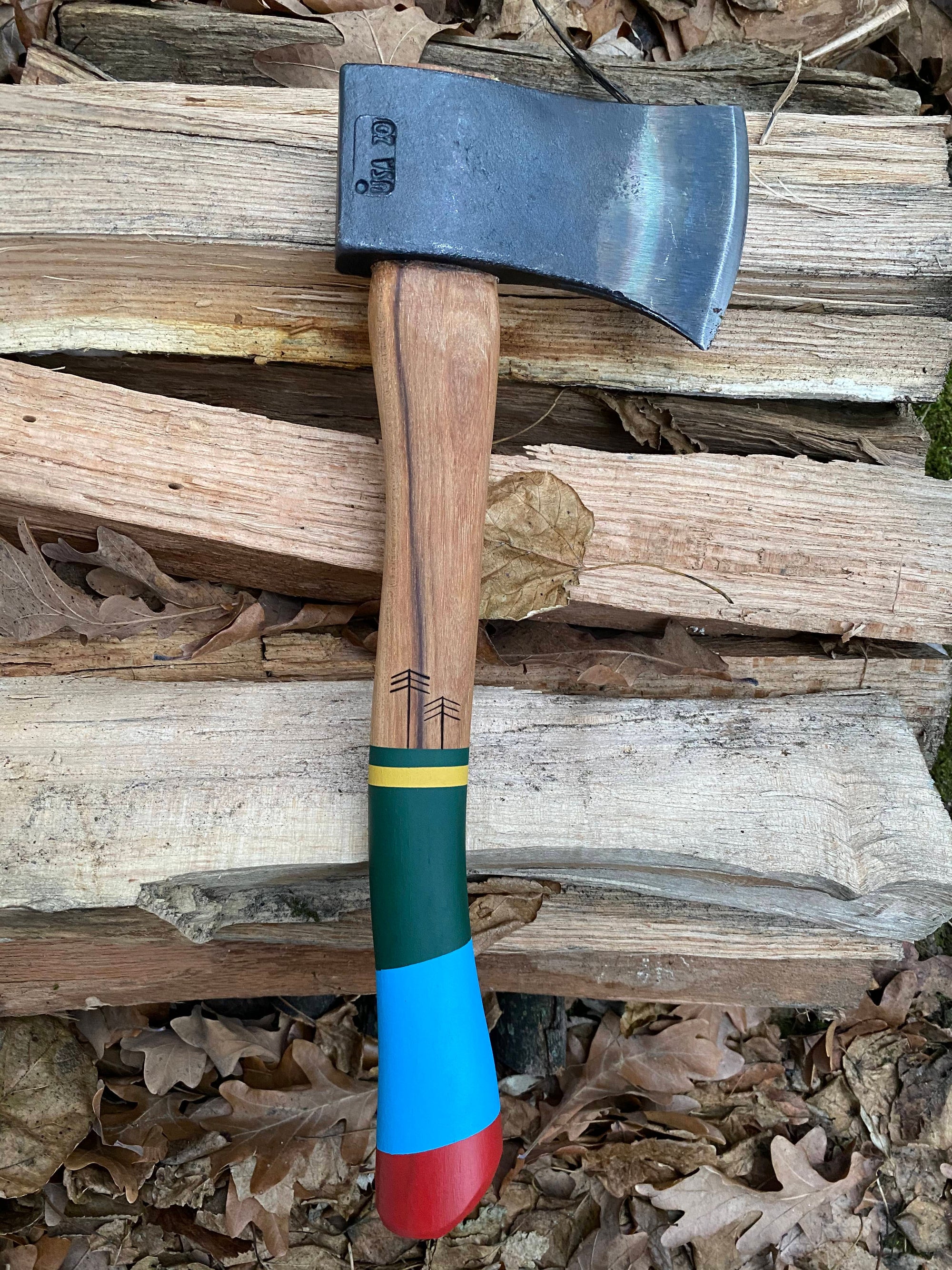 Small camping hatchet with steel head and colorful painted wooden handle on log background