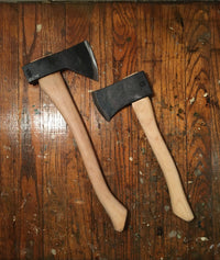 Two camping hatchets with black metal heads and natural wood handles on weathered surface