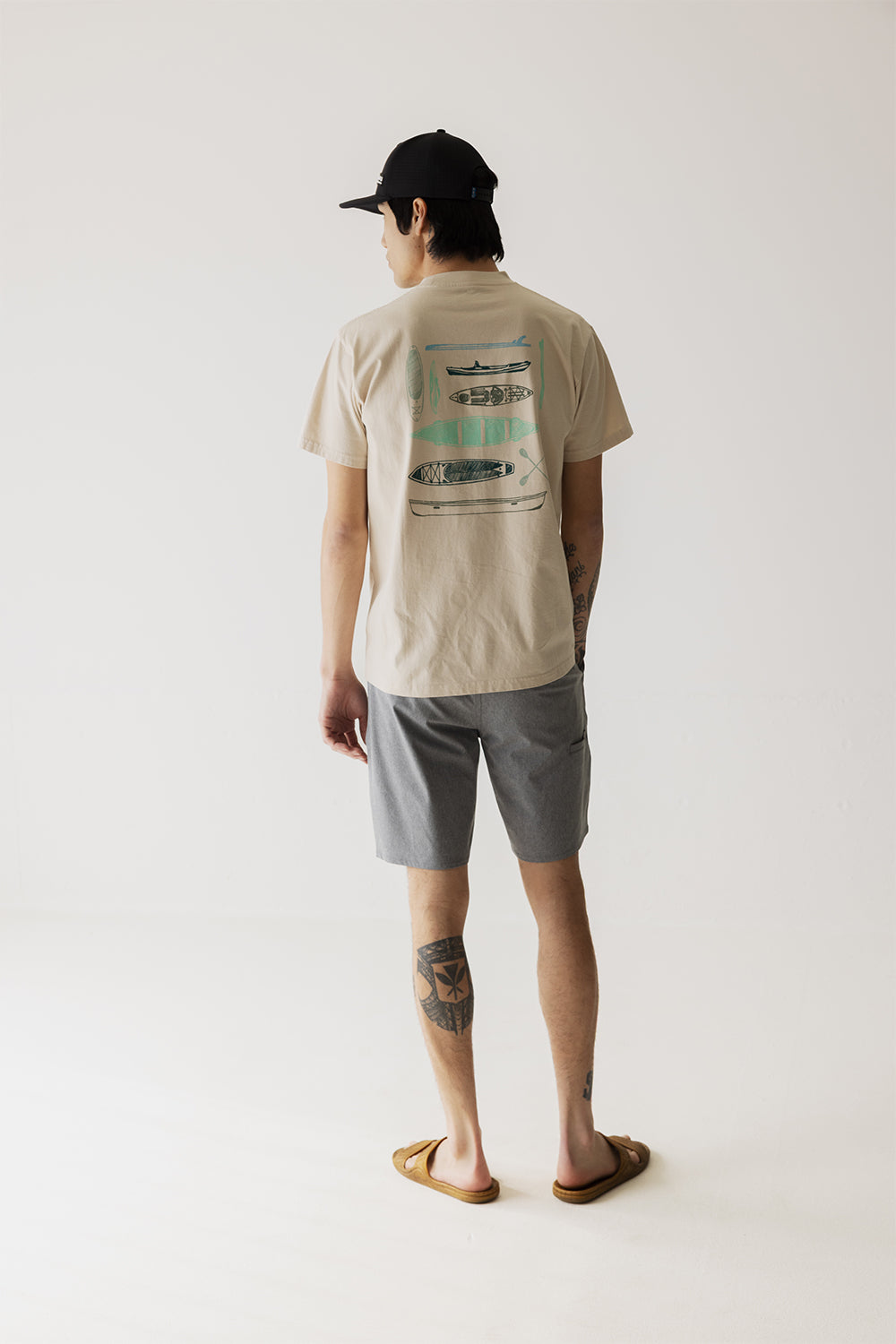 Back view of cream colored t-shirt with kayak illustrations worn with gray shorts
