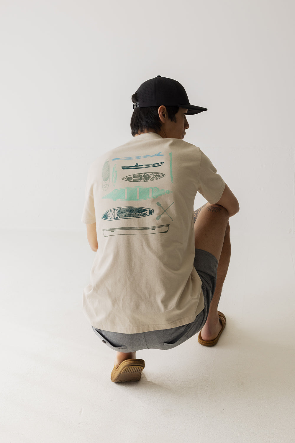 Men's short sleeve shirt with kayak illustrations on back, shown from behind on crouching model