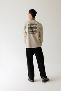 Back view of men's long-sleeve beige graphic tee with camping-themed print, worn with black pants