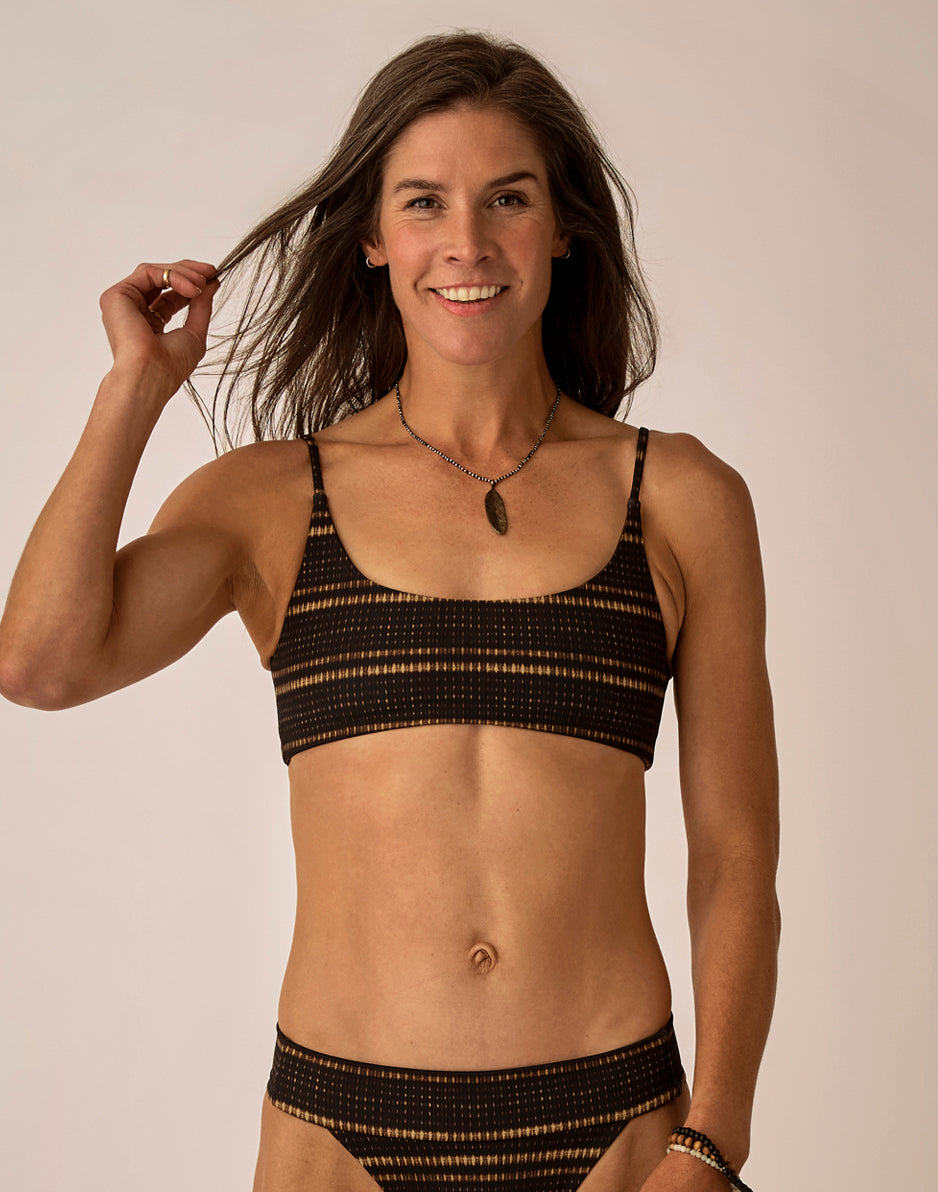 Women's black and gold striped bikini bralette top with thin straps, front view on model