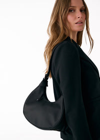 Black curved hobo bag worn on shoulder, side view showing smooth leather texture