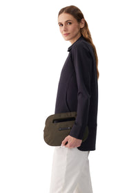 Woman holding an olive green oval-shaped crossbody clutch bag, side view