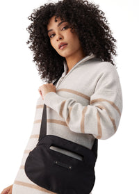 Black crossbody bag with top handle and shoulder strap, worn on model, side view