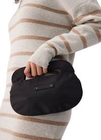 Small black rounded crossbody bag with top handle, held by model in striped sweater
