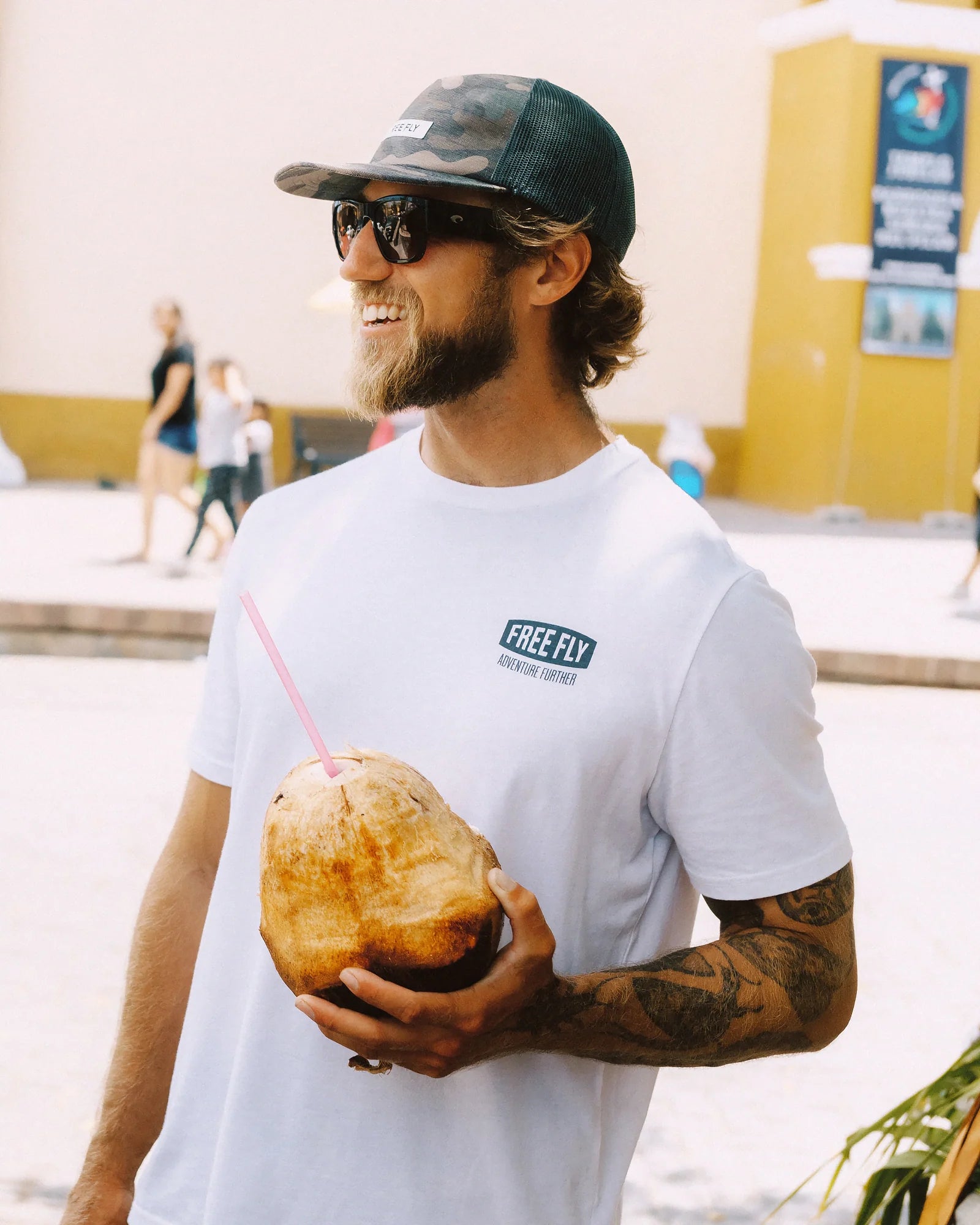 Man wearing white t-shirt with small chest logo, holding coconut drink outdoors