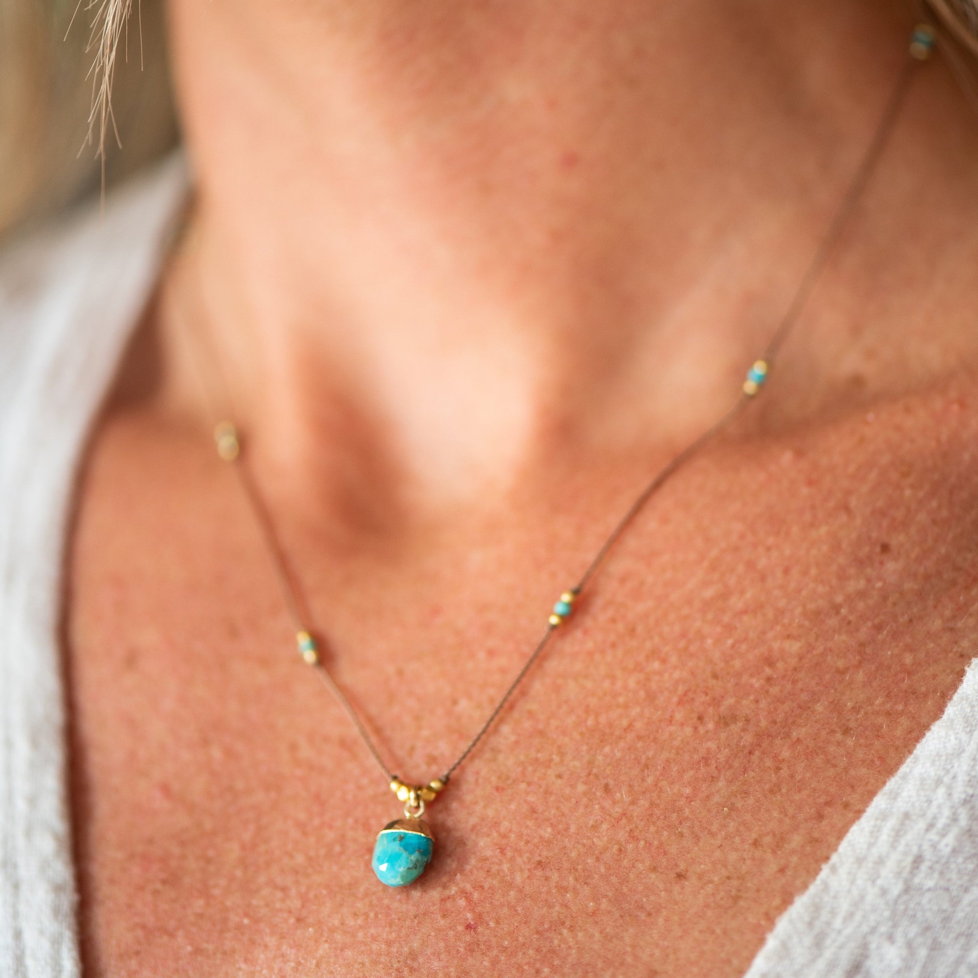 Delicate necklace with turquoise stone pendant and small beads on thin chain, worn on model