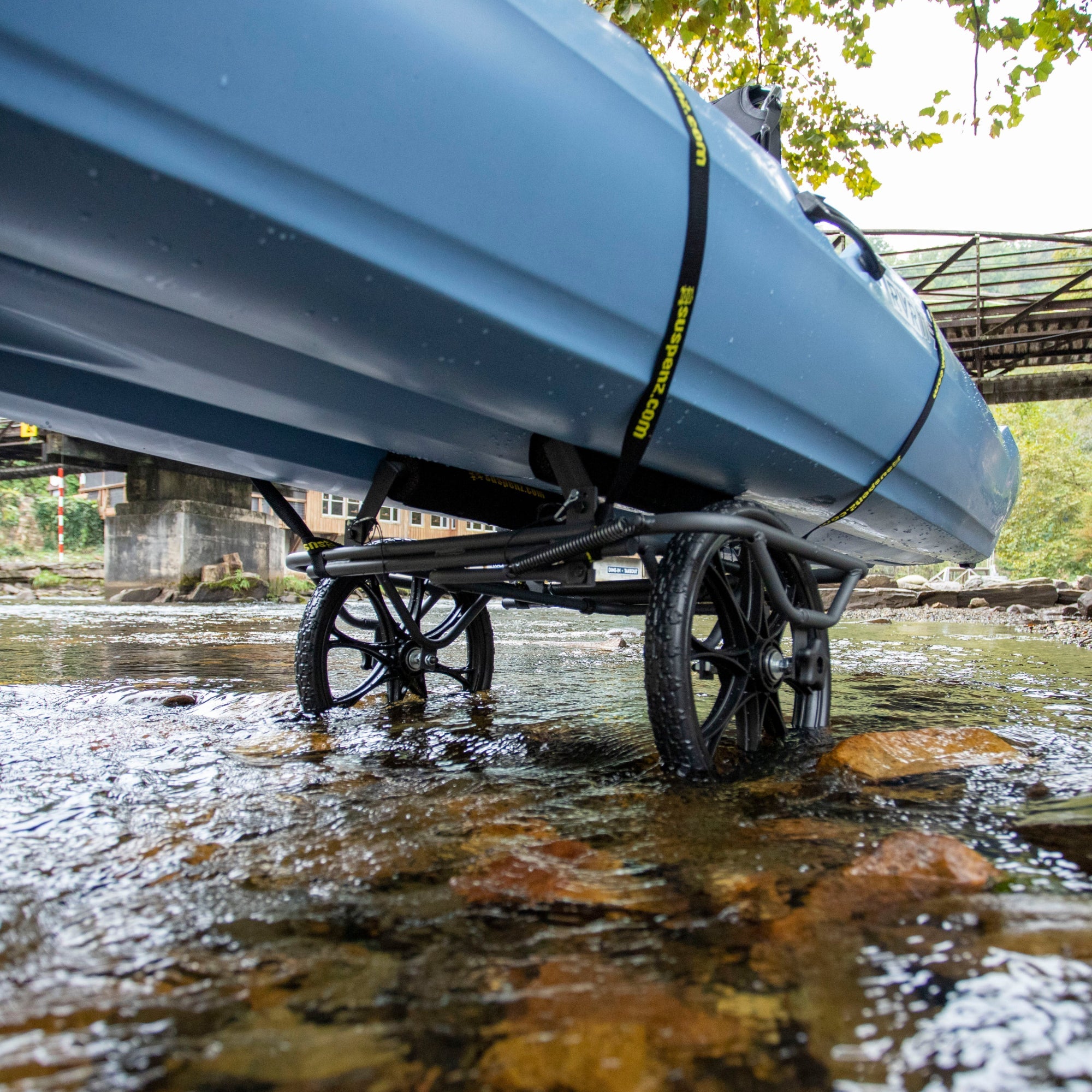 Blue kayak cart with airless wheels positioned in shallow water near bridge