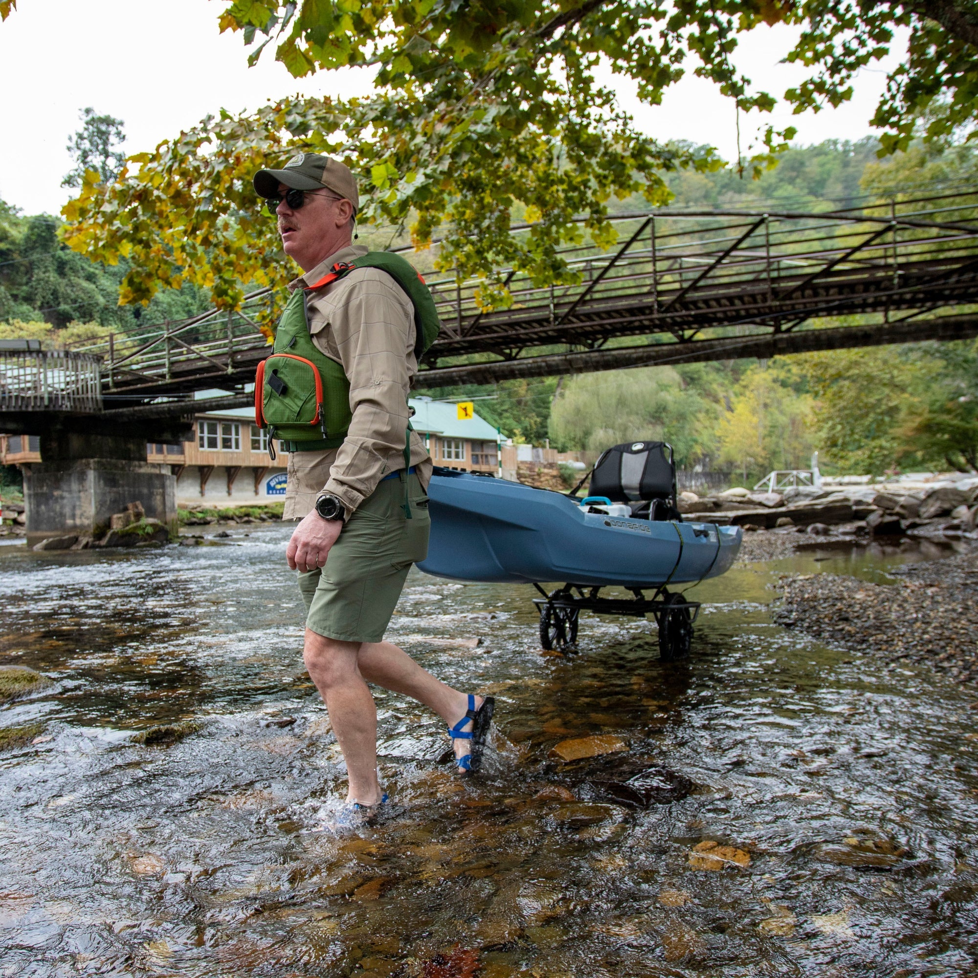 Blue kayak cart with wheels being pulled by angler through shallow water