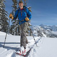 Person snowshoeing in winter with adjustable trekking poles, snowy mountain landscape background
