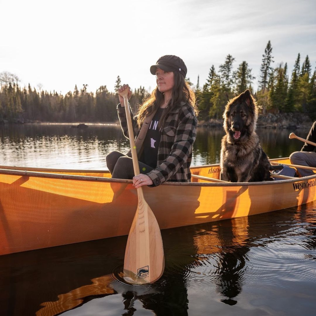 Wooden canoe paddle held by person in yellow canoe on lake with dog