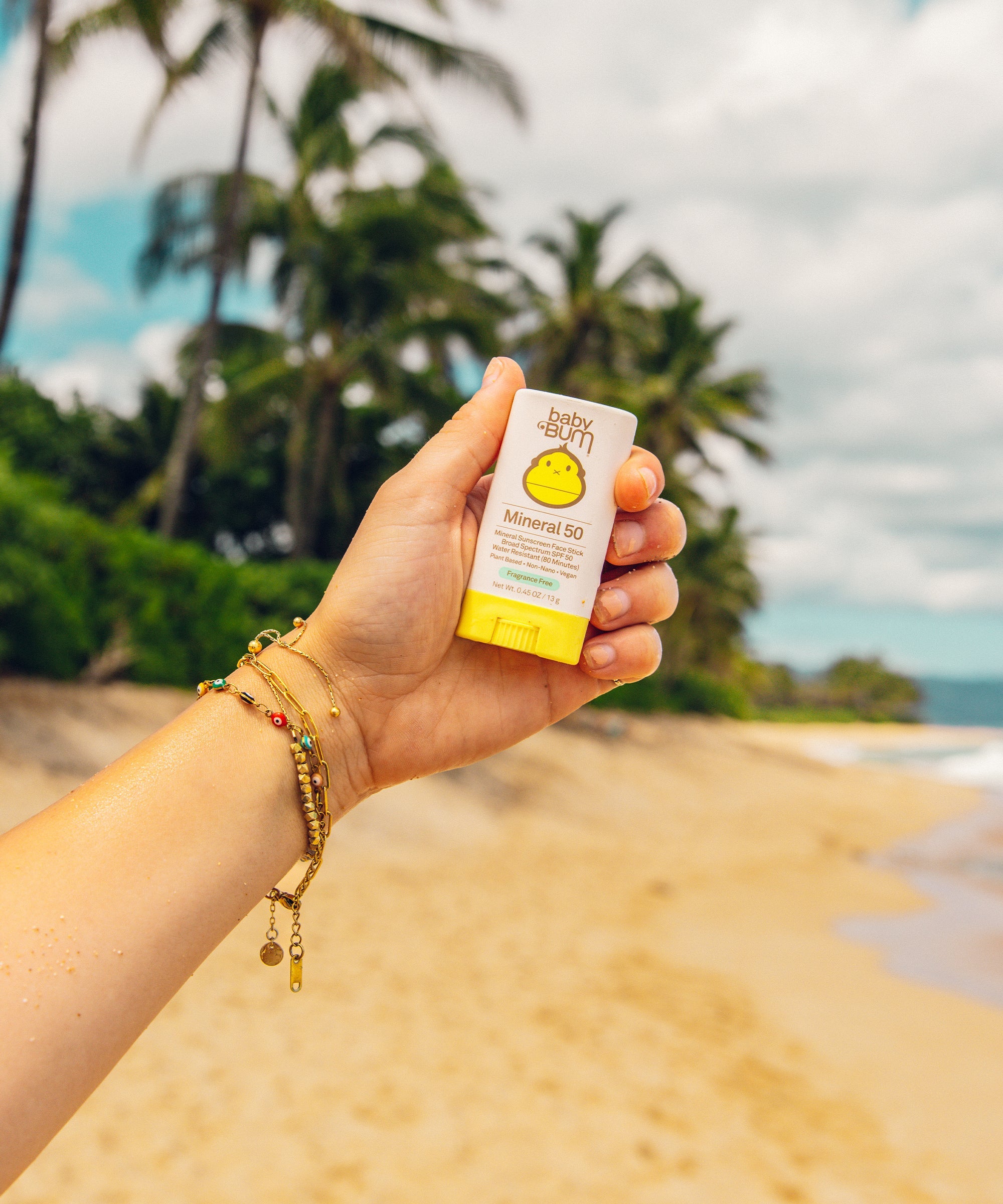 Hand holding small white and yellow mineral sunscreen stick on tropical beach background