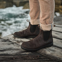 Chelsea boots in dark brown leather with elastic side panels, worn on weathered wooden dock