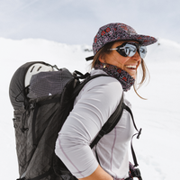 Woman hiking in snow wearing a floral patterned neckwarmer pulled up over chin, smiling