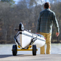 Kayak cart with yellow frame and black wheels holding white boat on launch ramp