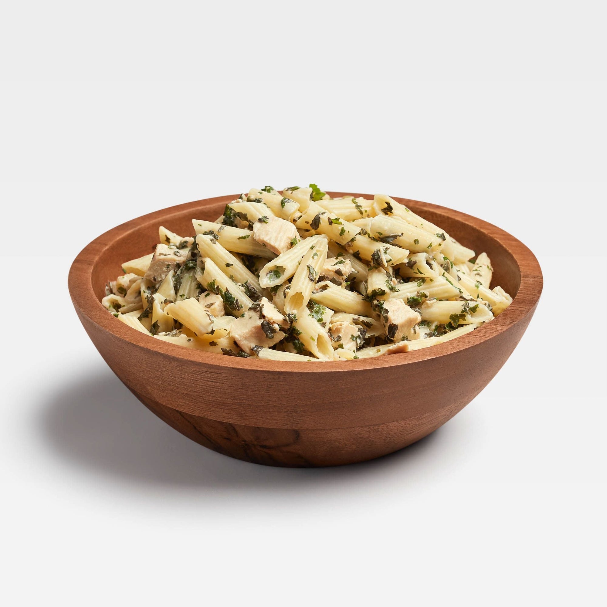 Prepared pasta dish with pesto sauce, chicken pieces, and herbs in wooden bowl