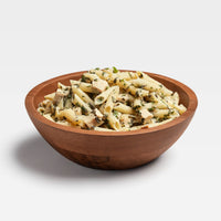Prepared pasta dish with pesto sauce, chicken pieces, and herbs in wooden bowl