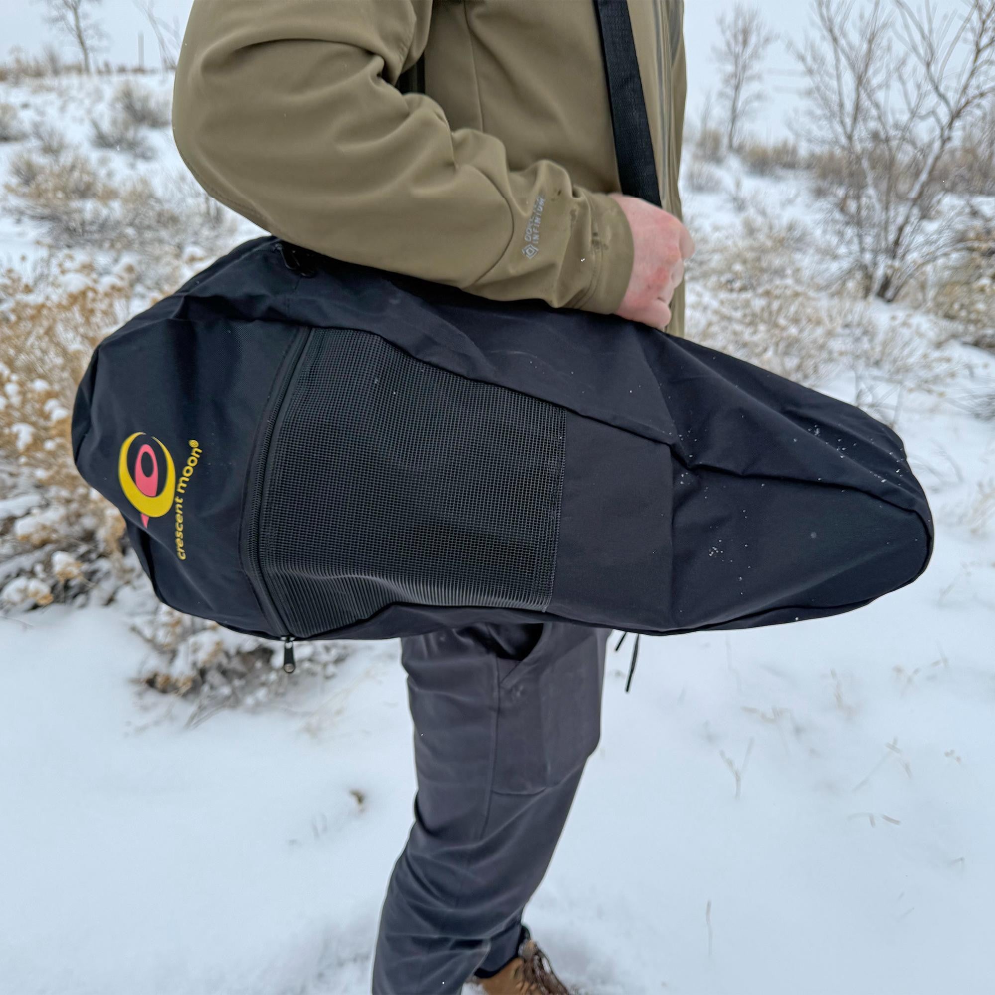 Navy snowshoe carry bag being held by person in snowy outdoor setting