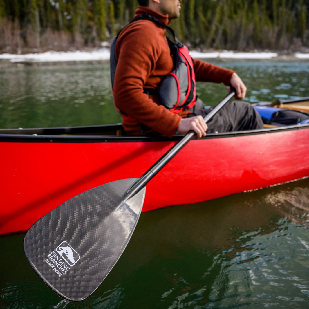 Carbon fiber pattern canoe paddle blade being held by kayaker in red canoe on water