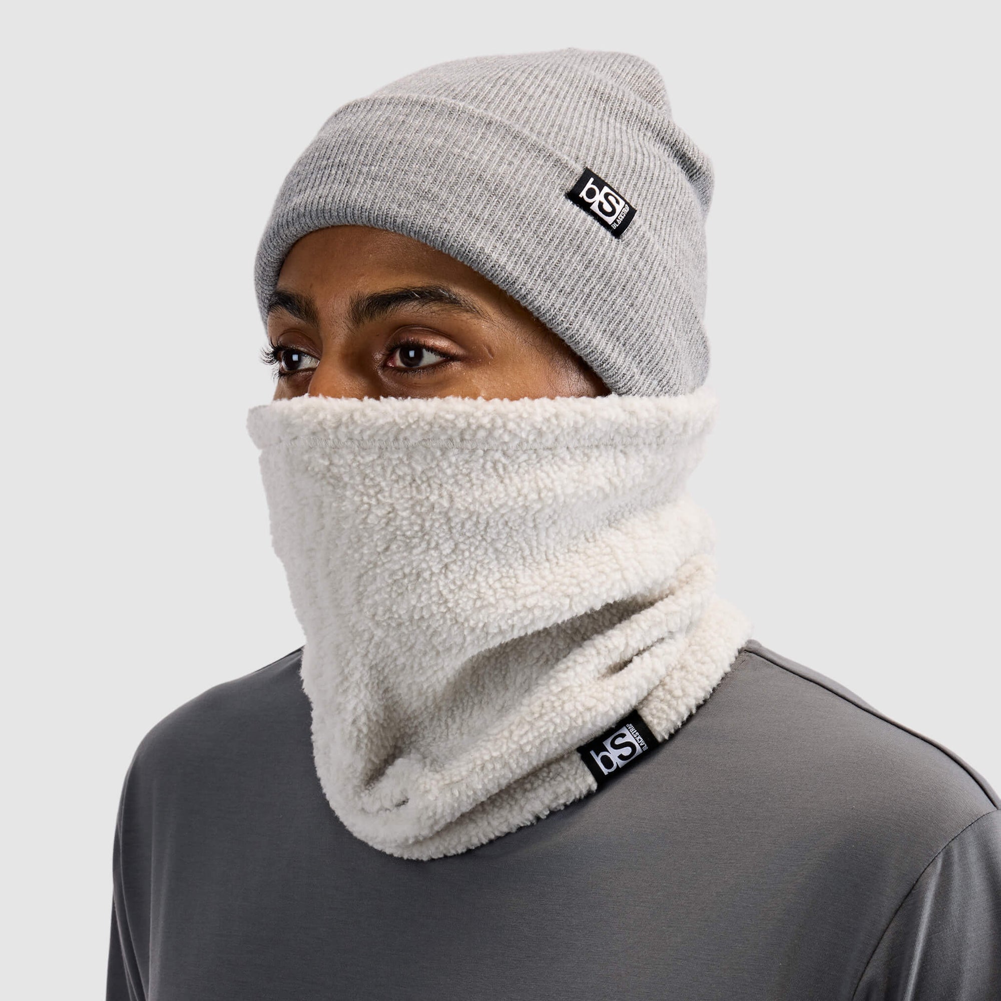 Sherpa fleece neck gaiter worn on model covering nose and chin, paired with gray beanie