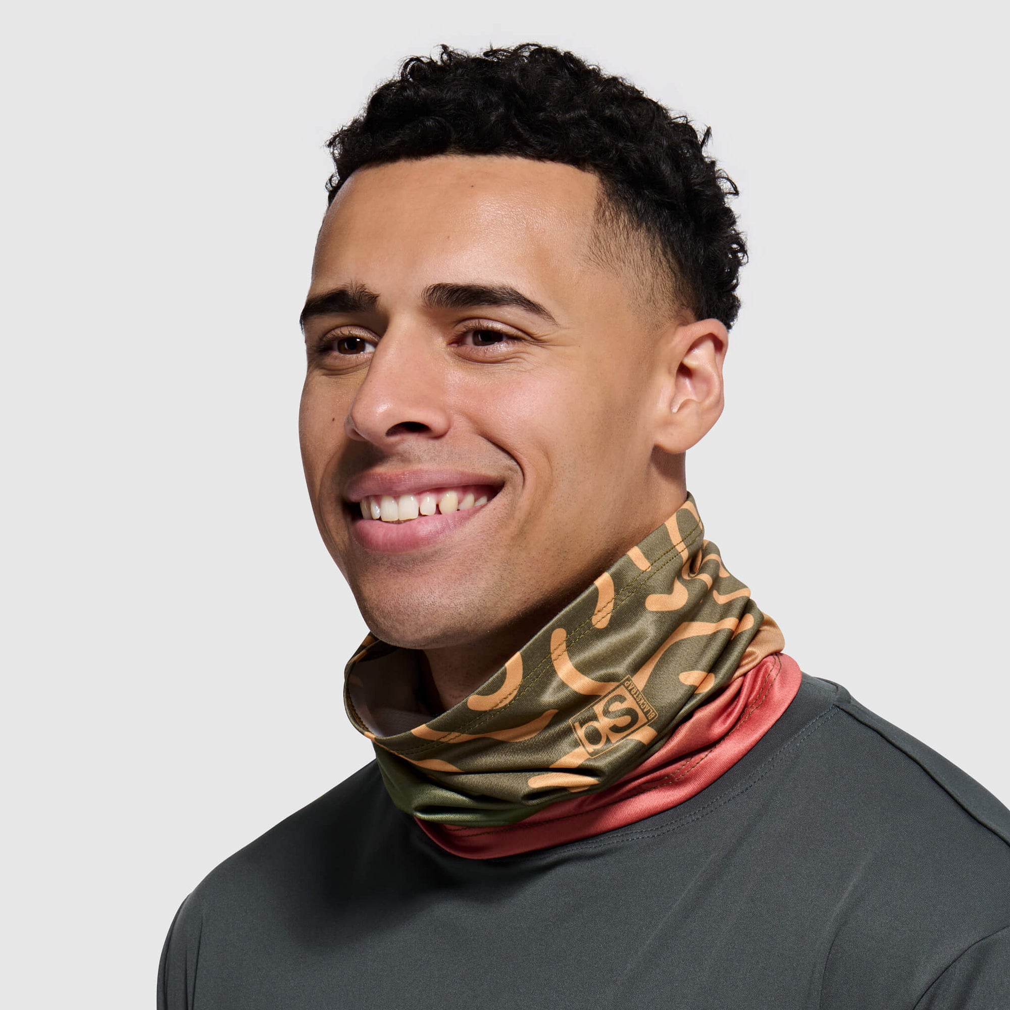 Camouflage patterned neck tube with coral accent band worn by smiling person