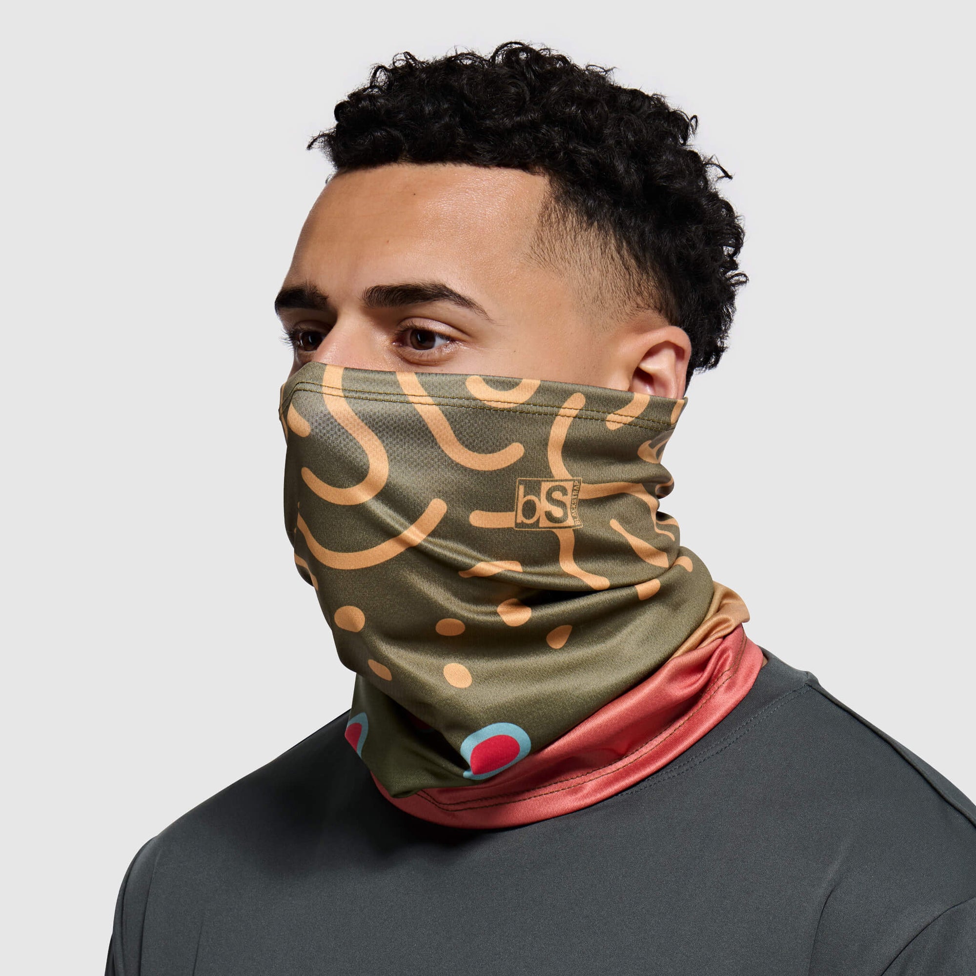 Olive green tube mask with trout pattern and colorful trim worn around neck and face