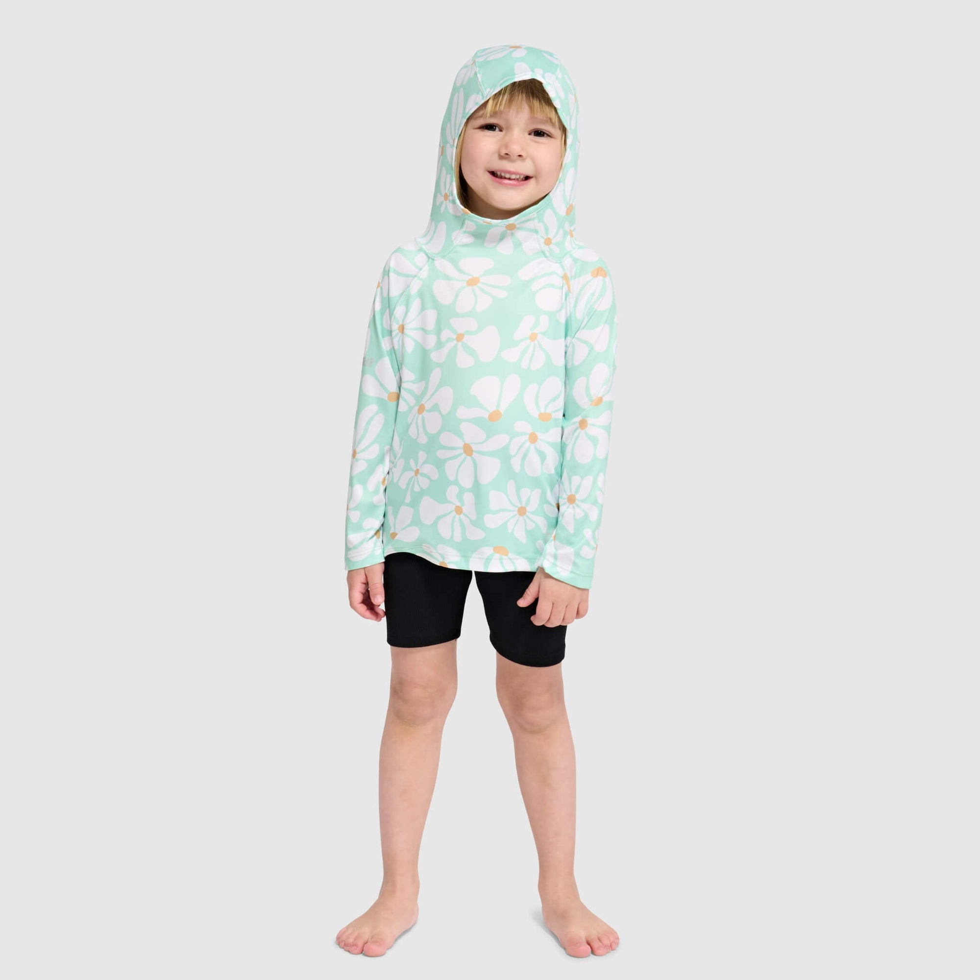 Child wearing mint green hooded sweatshirt with white daisy pattern and black shorts