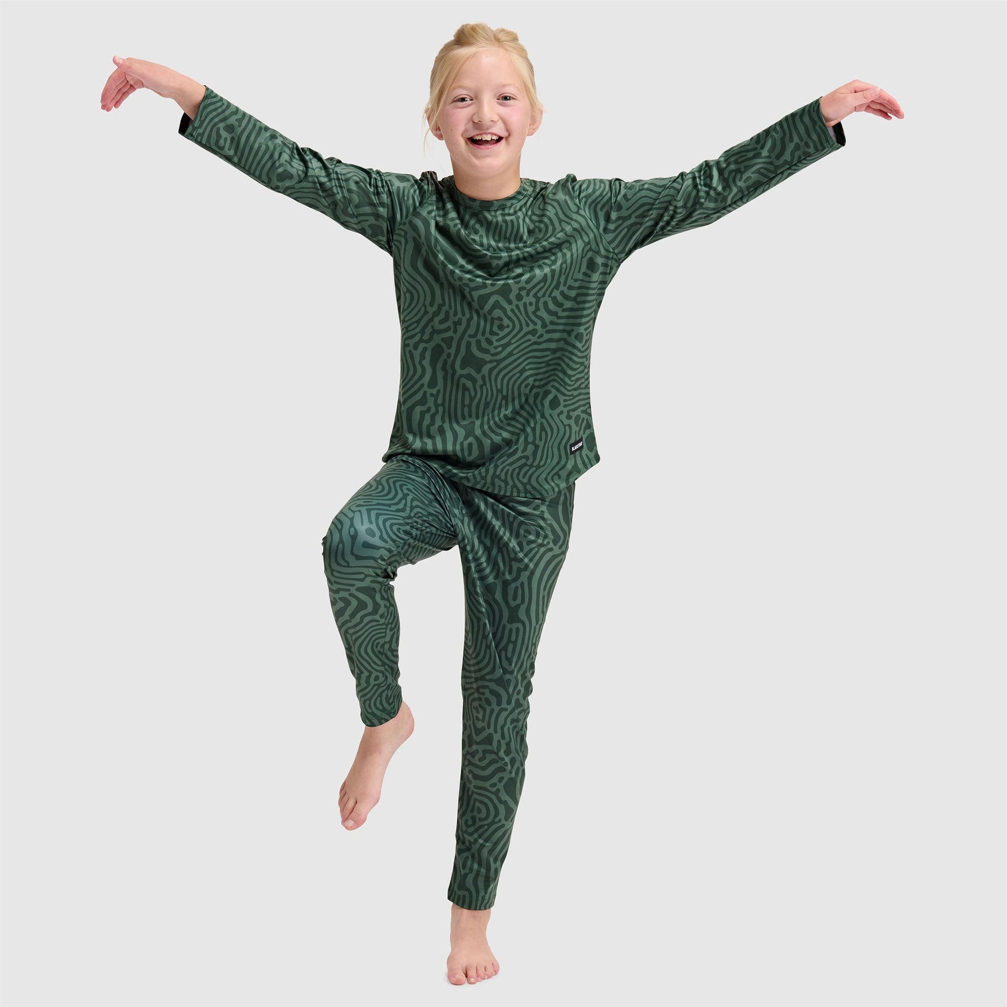 Child wearing green patterned base layer set with abstract swirl design, arms outstretched