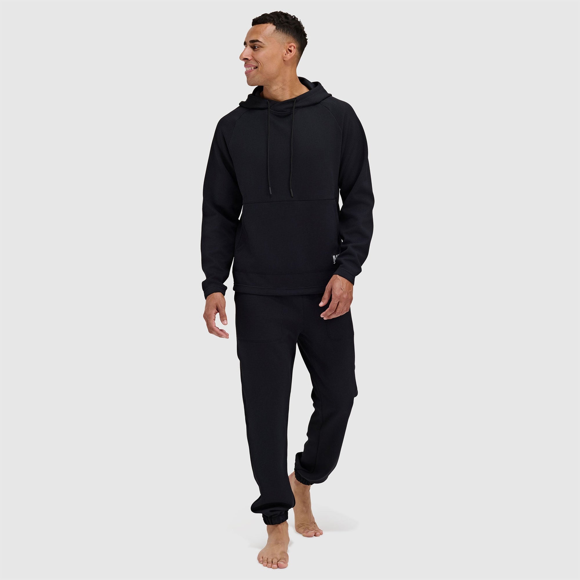 Black pullover hoodie with drawstrings and matching sweatpants worn by male model
