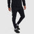 Men's slim-fit black jogger pants with zippered side pockets, worn with crocs, front angle view