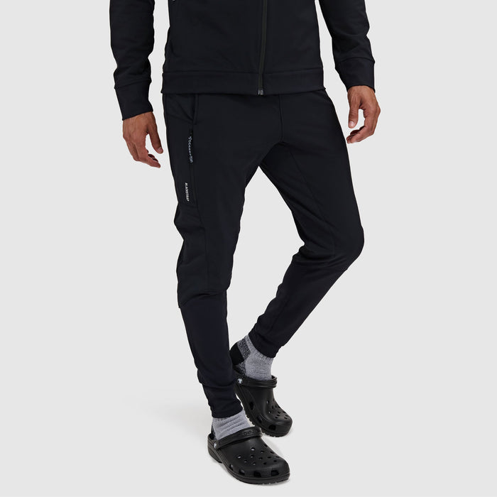 Men's slim-fit black jogger pants with zippered side pockets, worn with crocs, front angle view