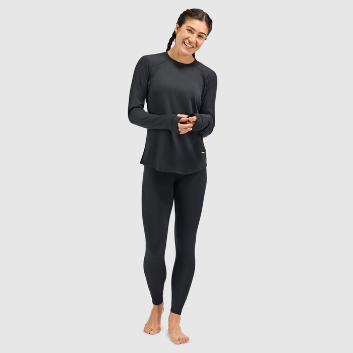 Women's long-sleeve crewneck base layer top with thumbholes, paired with black leggings, front view