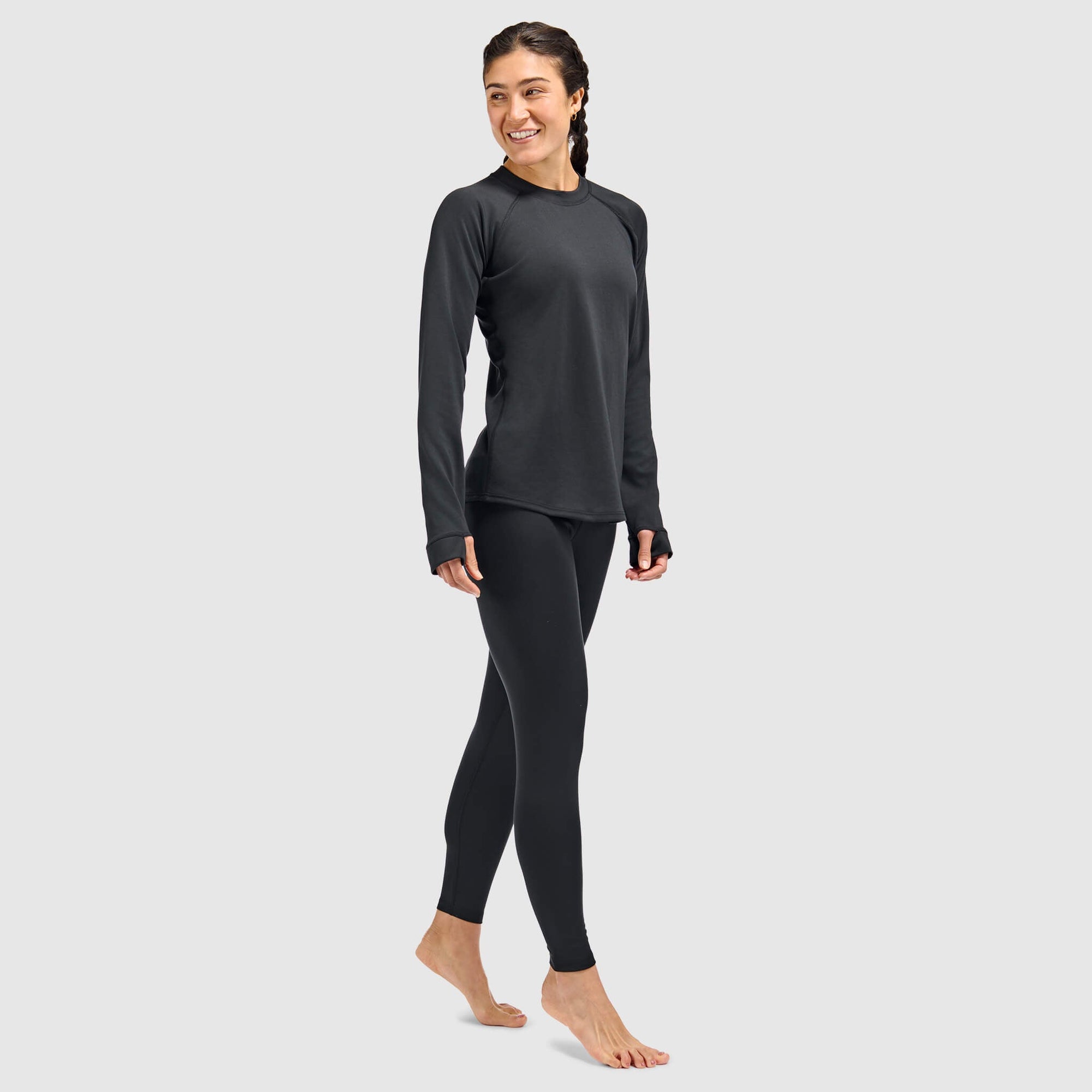 Women's long-sleeve crewneck base layer top with thumbholes, worn with matching leggings, front three-quarter view
