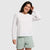Woman wearing white long-sleeve crewneck sweatshirt with light green shorts, smiling pose