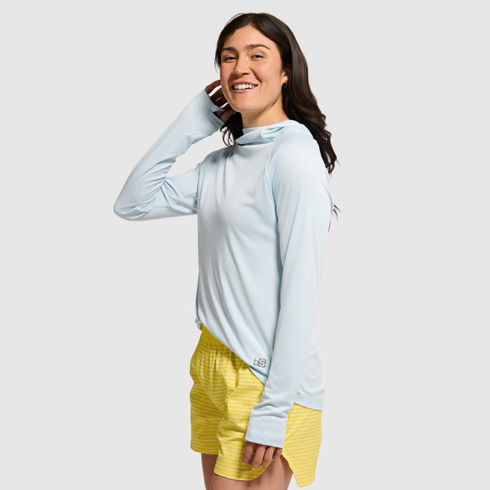 Woman wearing light blue hoodie with yellow shorts, smiling and posing against white background