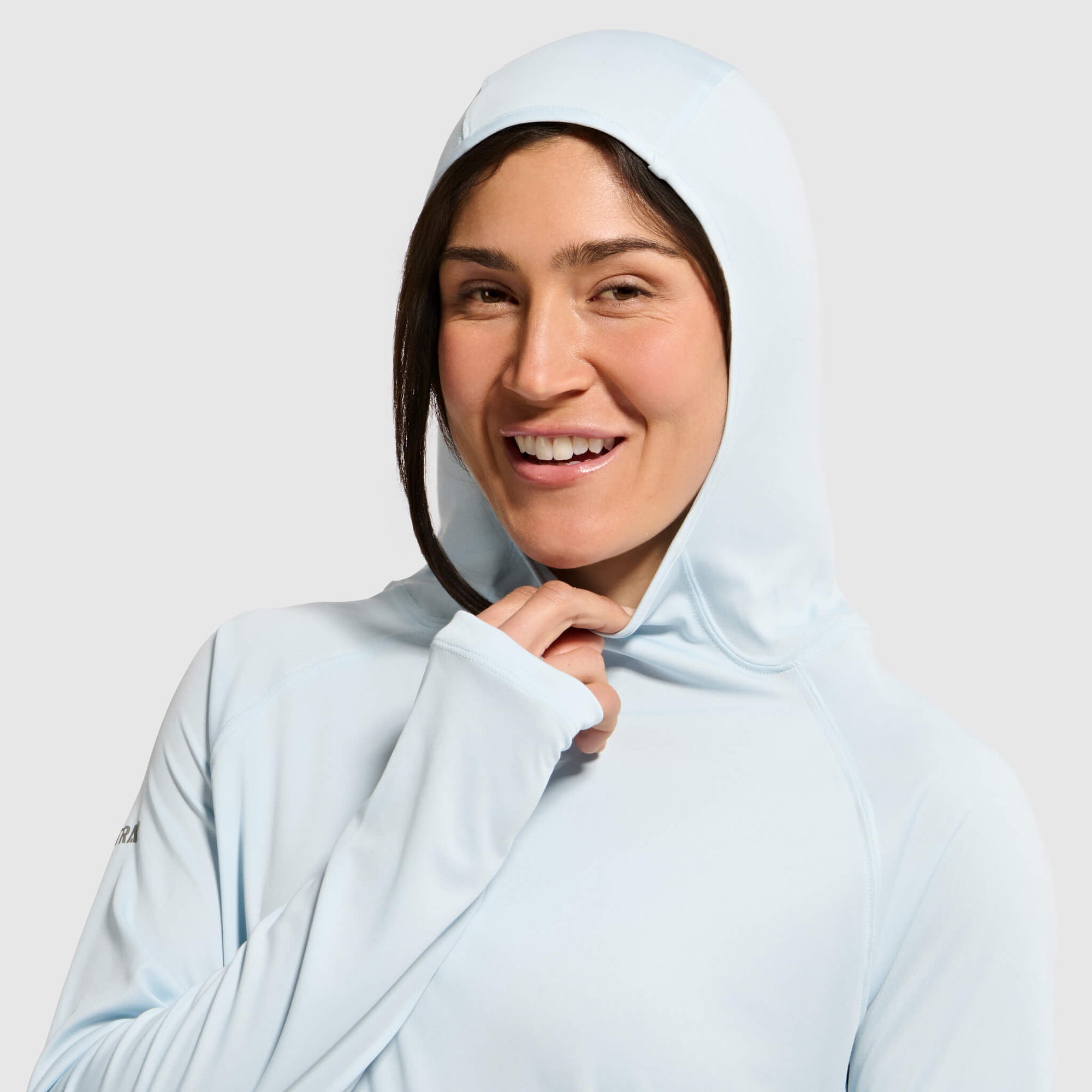 Light blue hoodie with hood up worn by smiling woman against white background