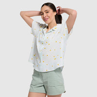 White camp shirt with yellow polka dot pattern worn by woman with hands behind head