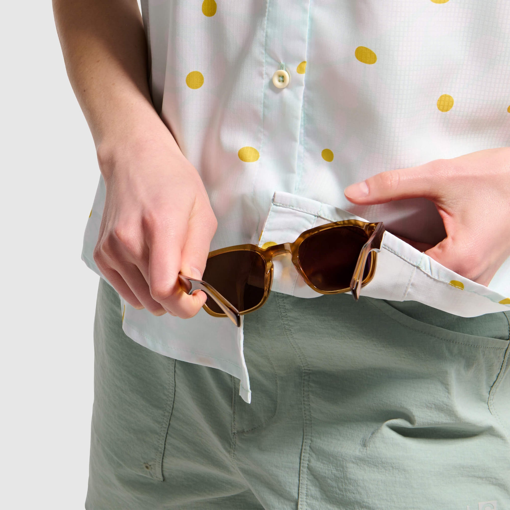 White button-up camp shirt with yellow polka dots, shown with person cleaning sunglasses