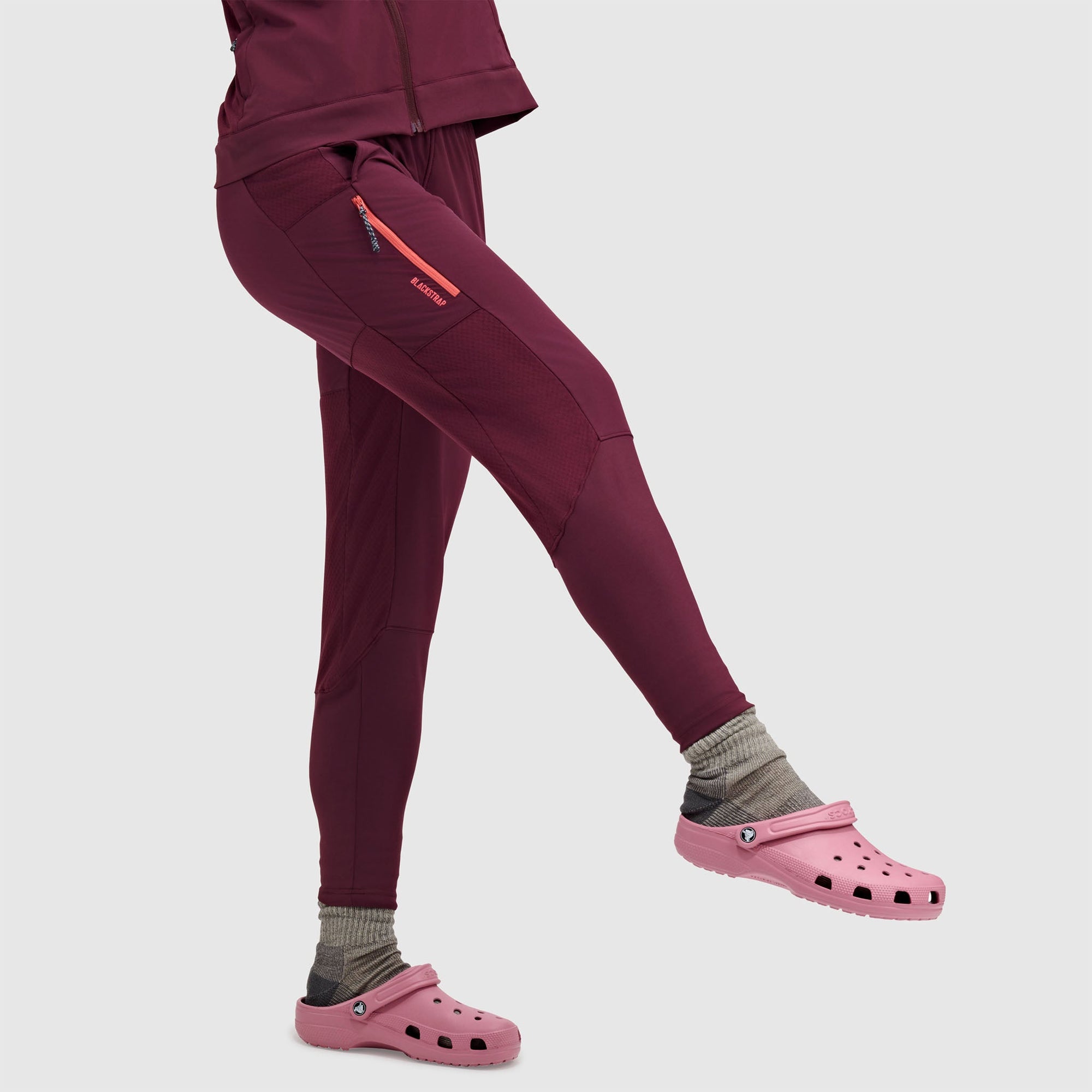Deep red fleece leggings with side pockets and orange zipper details, side view