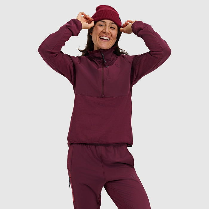 Woman wearing burgundy half-zip pullover jacket and matching pants with knit beanie, smiling pose