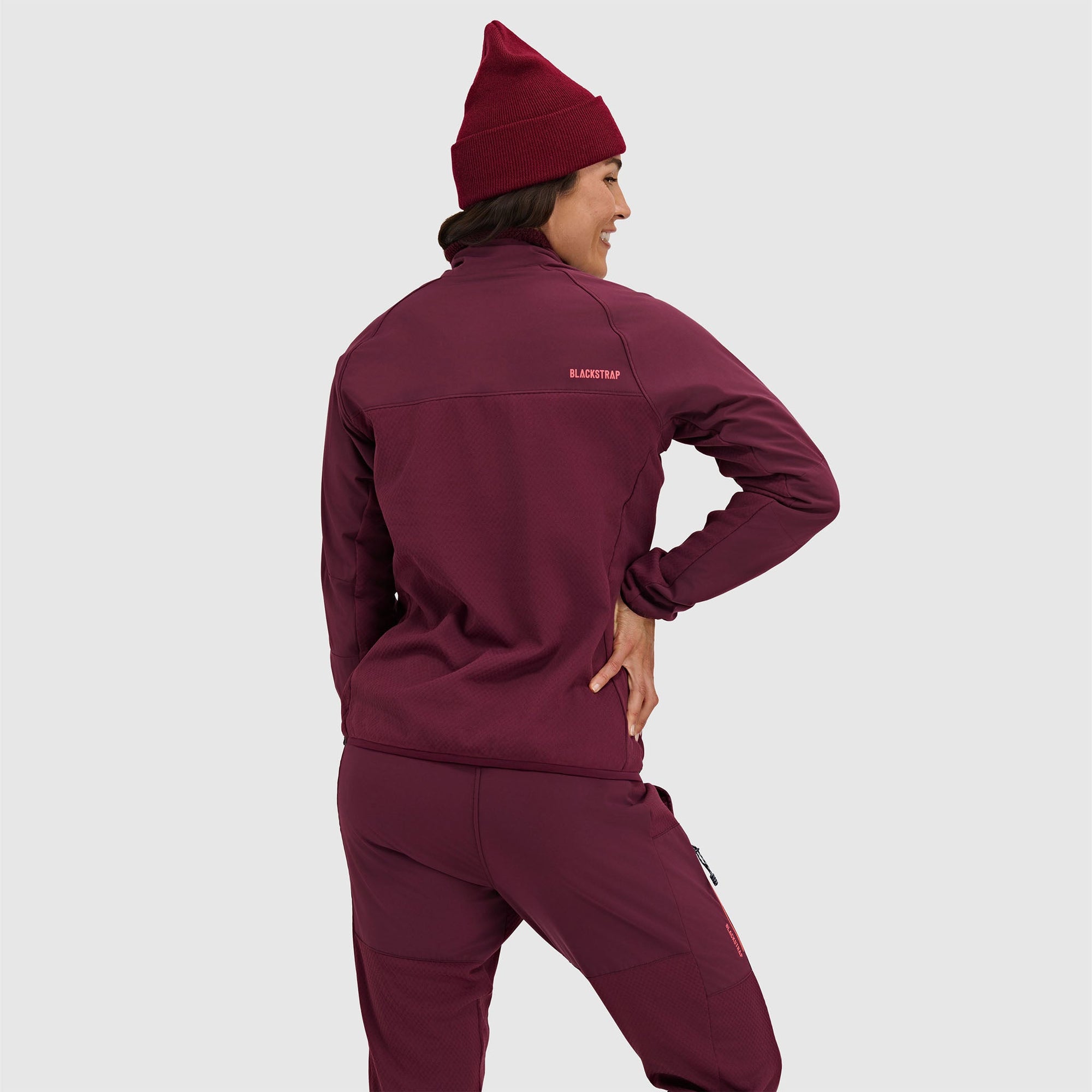 Woman wearing deep burgundy half-zip fleece pullover and matching beanie, shown from back view