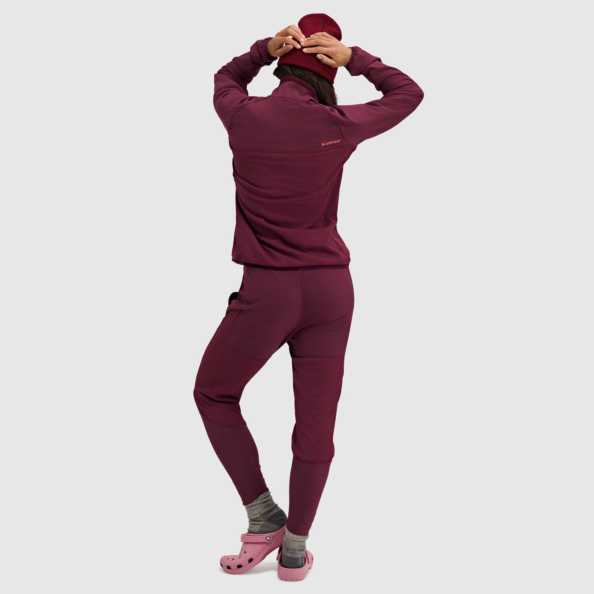 Woman wearing burgundy fleece pullover jacket and matching leggings, back view with hood up