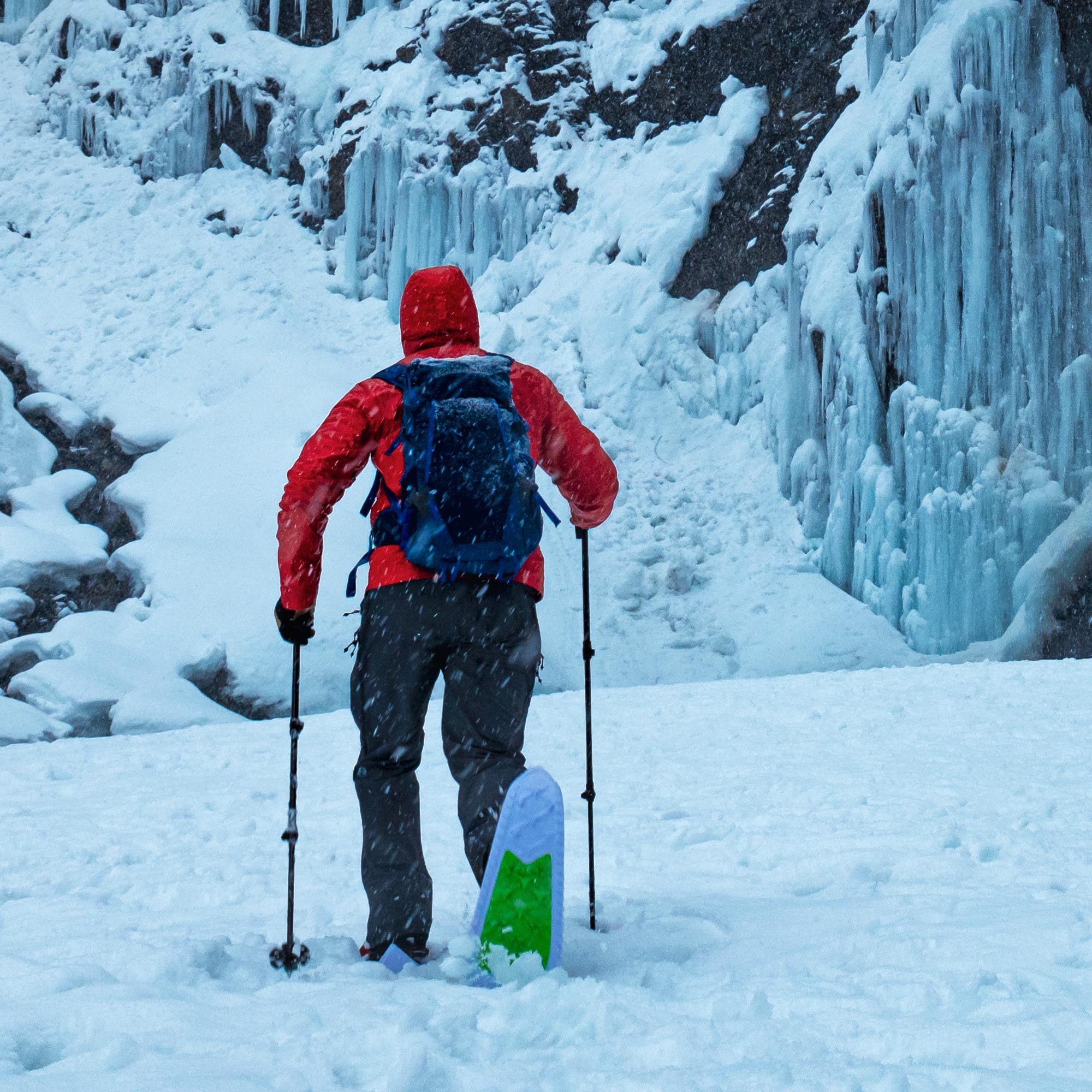Person using black adjustable trekking poles while skiing through snowy winter landscape with ice formations